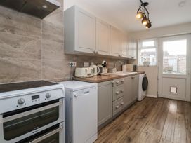 A kitchen with appliances and cabinets along one wall and a door with window blinds at Lychgate View Cottage in Aldbrough
