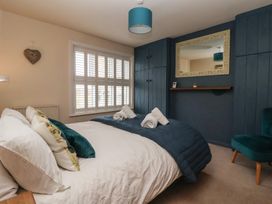 A bedroom with a bed with pillows and rolled towels next to a window with shutters and built in wardrobes at Lychgate View Cottage in Aldbrough