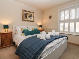 A bedroom with a white bed frame blue bedding rolled towels two wooden bedside tables with lamps and window shutters at Lychgate View Cottage in Aldbrough