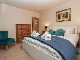 A bedroom with a double bed with pillows and rolled towels a wooden chest of drawers a wooden door a green armchair and bedside tables with lamps at Lychgate View Cottage in Aldbrough