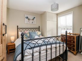 A bedroom with a black metal bed frame a wooden nightstand with a lamp a chest of drawers and a window with blinds at Lychgate View Cottage in Aldbrough