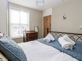 A bedroom with a bed with blue pillows and rolled white towels a wooden dresser a floor mirror and a window with blinds at Lychgate View Cottage in Aldbrough