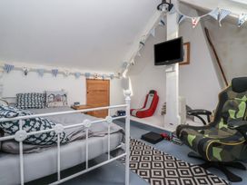 A bedroom with a white metal bed frame pillows a gaming chair a wall-mounted TV and bunting at Lychgate View Cottage in Aldbrough