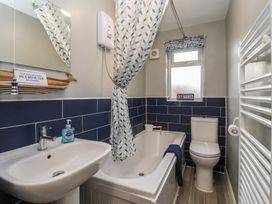 A bathroom with a bathtub shower toilet sink and blue tiled walls at Lychgate View Cottage in Aldbrough