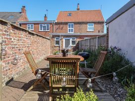 An outdoor patio area with a wooden table and chairs a barbecue and string lights at Lychgate View Cottage in Aldbrough