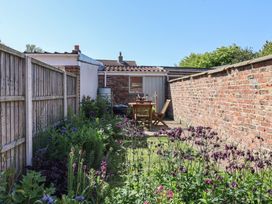 A narrow garden with flowers wooden fence on one side and brick wall on the other Lychgate View Cottage Aldbrough