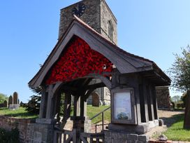A wooden lychgate with red flowers decorating the roof below a stone clock tower at Lychgate View Cottage in Aldbrough
