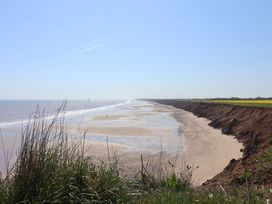 A sandy beach with cliffs and sea viewed from a grassy cliff at Lychgate View Cottage in Aldbrough