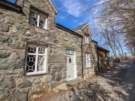 A stone cottage with white framed windows and a white door beside a tree-lined road at Clywedog Cottage in Dolgellau