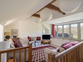 A living room with sofas a patterned rug wooden beams and large windows at Clywedog Cottage in Dolgellau