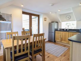 A kitchen with a wooden dining table and chairs a refrigerator and a countertop with a sink and a clock on the wall at Clywedog Cottage in Dolgellau