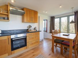 A kitchen with wooden cabinets, an oven, a dining table with four chairs, and large windows with curtains at Clywedog Cottage in Dolgellau