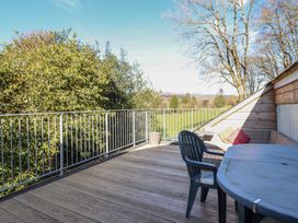 An outdoor balcony with wooden flooring a table and chairs overlooking trees and fields at Clywedog Cottage in Dolgellau