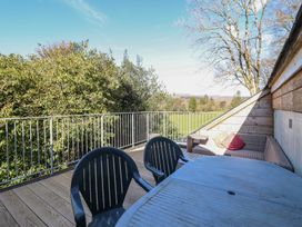 A wooden deck with plastic chairs and a wicker sofa with cushions overlooking trees and a grassy field at Clywedog Cottage in Dolgellau