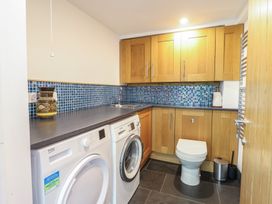 A utility room with a washing machine, dryer, toilet, sink, wooden cabinets, and blue tiled backsplash at Clywedog Cottage in Dolgellau