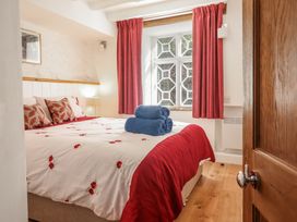 A bedroom with a bed covered in white and red floral bedding blue towels on the bed red curtains wooden floor and a window at Clywedog Cottage in Dolgellau