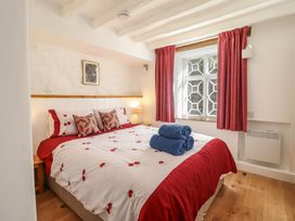 A bedroom with a double bed red and white bedding blue towels on the bed red curtains on the window and wooden floor at Clywedog Cottage in Dolgellau