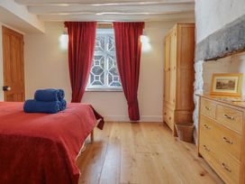 A bedroom with a red bedspread blue towels wooden dresser and wardrobe red curtains on window at Clywedog Cottage in Dolgellau