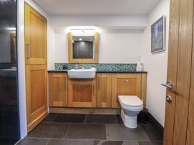 A bathroom with a toilet a sink with wooden cabinets a mirror and a framed picture on the wall at Clywedog Cottage in Dolgellau