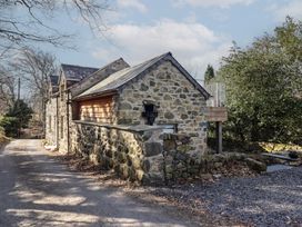 A stone cottage beside a gravel road with trees and bushes nearby at Clywedog Cottage in Dolgellau