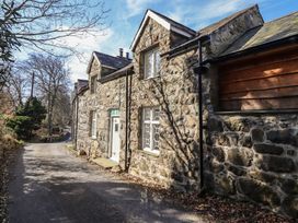 Stone cottage with white windows and door next to a narrow road surrounded by trees at Clywedog Cottage in Dolgellau