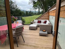 An outdoor wooden deck with wicker seating a round table with a red polka dot tablecloth and a view of green fields at Clywedog Cottage in Dolgellau