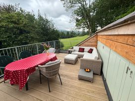 An outdoor wooden deck with a red polka dot tablecloth on a table surrounded by chairs and a wicker sofa set with cushions at Clywedog Cottage in Dolgellau