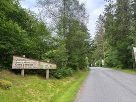 A road with trees on both sides and a wooden sign welcoming visitors to Goedy Brenin Visitor Centre