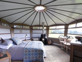 A bedroom with a bed stove and dining table inside a round cabin at Caban Llwynon Tresillian Wood near Llantwit Major