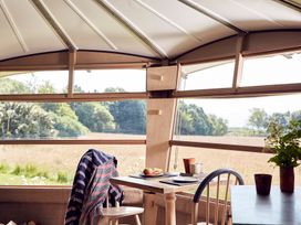 A dining table set with plates and cups inside a room with large windows overlooking a field at Caban Llwynon in Tresillian Wood near Llantwit Major