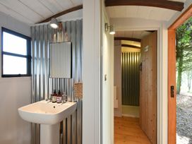 A bathroom sink with a mirror and soap dispensers next to an open wooden door showing a metal wall at Caban Llwynon in Tresillian Wood near Llantwit Major