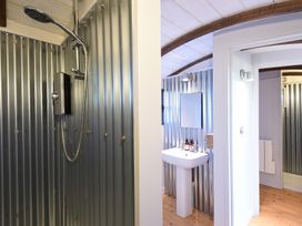 A bathroom with a shower area, pedestal sink, wall mirror, and corrugated metal walls at Caban Llwynon Tresillian Wood near Llantwit Major