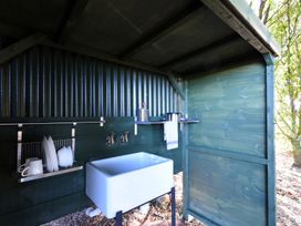 An outdoor sink setup with a white basin dishes drying rack and utensils at Caban Llwynon Tresillian Wood near Llantwit Major