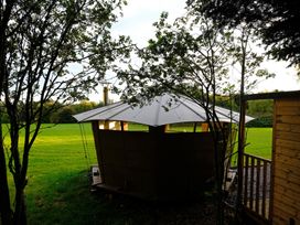 A wooden outdoor structure with a white roof surrounded by trees and grass at Caban Llwynon in Tresillian Wood near Llantwit Major