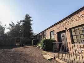 Stone building with black doors and windows surrounded by gravel and trees at Periwinkle Akeld near Wooler