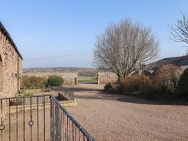 An outdoor courtyard area with stone walls trees bushes and a gravel driveway at Periwinkle in Akeld near Wooler