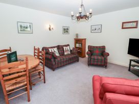 A living room with a dining table and chairs tartan sofas a television and framed pictures on walls at Periwinkle Akeld near Wooler