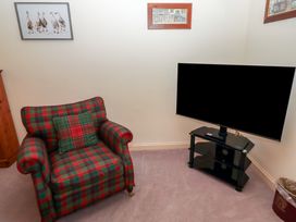 A room with a plaid armchair a flat screen TV on a black stand and framed artwork on the walls at Periwinkle in Akeld near Wooler