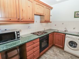 A kitchen with wooden cabinets a microwave electric stove oven washing machine and a sink at Periwinkle in Akeld near Wooler