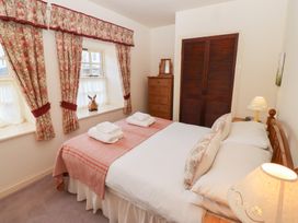 A bedroom with a bed covered in white and pink bedding next to a nightstand with a lamp floral curtains on windows and wooden closet doors at Periwinkle Akeld near Wooler