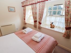 A bedroom with a bed and folded towels on a pink bedspread next to windows with floral curtains and a rabbit figurine on the window sill at Periwinkle in Akeld near Wooler
