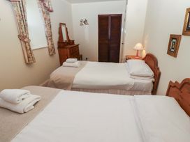 A bedroom with two single beds a wooden dresser with mirror a bedside table with lamp and a window with curtains at Periwinkle Akeld near Wooler