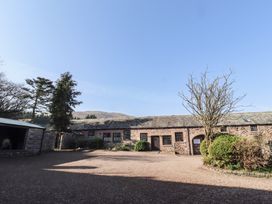 The exterior of a stone building with multiple windows and doors with trees and shrubs in front at Periwinkle in Akeld near Wooler