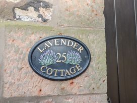 A black oval house sign with lavender illustrations and the number 25 mounted on a stone wall at Lavender cottage in Akeld near Wooler