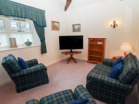 A living room with plaid armchairs and couch a television on a wooden table a wooden bookshelf and green plaid curtains at Lavender cottage in Akeld near Wooler