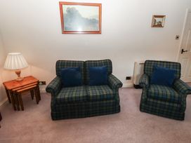 A sitting room with a checked sofa and armchair with blue cushions a wooden lamp table with lamp and paintings on the wall at Lavender cottage Akeld near Wooler