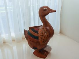 A wooden duck figurine with painted wings standing on a white surface near a window with sheer white curtains at Lavender cottage in Akeld near Wooler