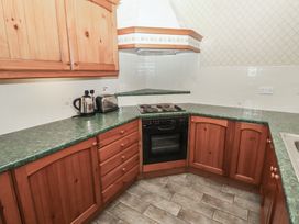 A kitchen with wooden cabinets green countertops an electric stove oven a toaster and a kettle at Lavender cottage in Akeld near Wooler
