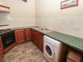 A kitchen with wooden cabinets a green countertop a sink a washing machine an oven and tiled walls at Lavender cottage Akeld near Wooler