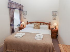 A bedroom with a double bed with beige blanket and towels on it flanked by two wooden bedside tables with lamps and curtains on a window at Lavender cottage in Akeld near Wooler